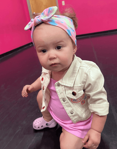 Baby girl is wearing a baby headband featuring a tie dye pattern for little girls from By Bella Boutique. Baby girl is wearing a baby headband featuring a tie dye pattern for little girls from By Bella Boutique.