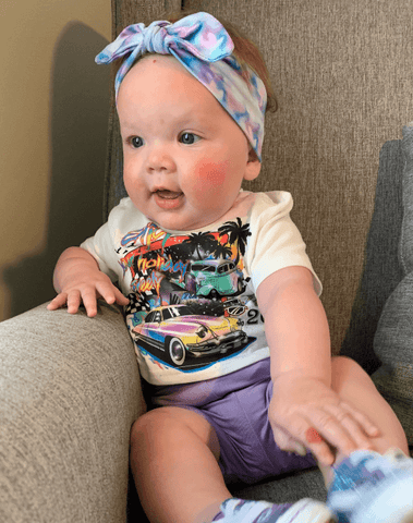 Baby girl is wearing a knotted headband featuring a tie dye pattern for little girls from By Bella Boutique. Baby girl is wearing a knotted headband featuring a tie dye pattern for little girls from By Bella Boutique.