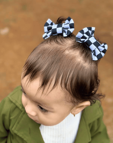 Toddler girl is wearing a set of two hair clips featuring a white checkerboard pattern for little girls from By Bella Boutique. Toddler girl is wearing a set of two hair clips featuring a white checkerboard pattern for little girls from By Bella Boutique.