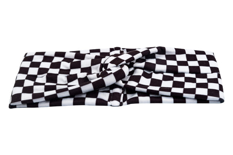 A wide turban headband for women featuring a white checkerboard pattern from By Bella Boutique. A wide turban headband for women featuring a white checkerboard pattern from By Bella Boutique.