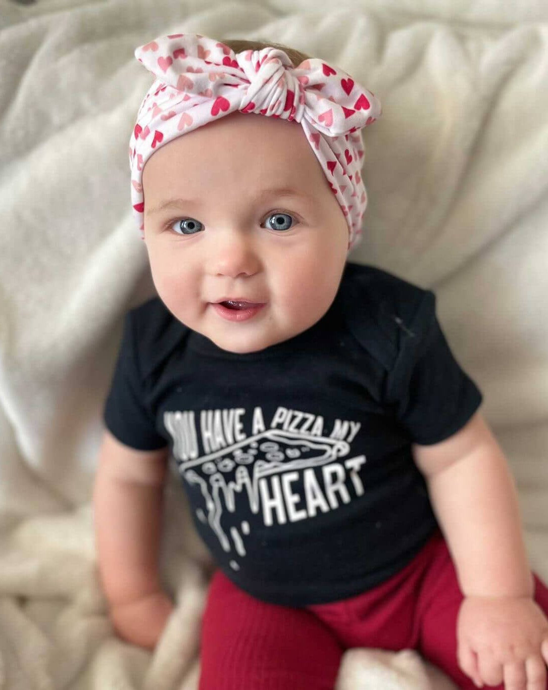 Baby girl is wearing a heart print knot headband for little girls from By Bella Boutique. Baby girl is wearing a heart print knot headband for little girls from By Bella Boutique.