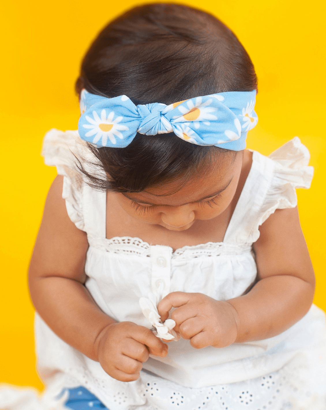 Baby girl is wearing a knotted head wrap featuring a daisy pattern for little girls from By Bella Boutique. Baby girl is wearing a knotted head wrap featuring a daisy pattern for little girls from By Bella Boutique.