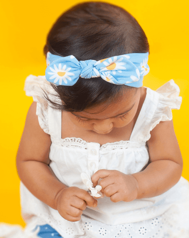 Baby girl is wearing a knotted head wrap featuring a daisy pattern for little girls from By Bella Boutique. Baby girl is wearing a knotted head wrap featuring a daisy pattern for little girls from By Bella Boutique.