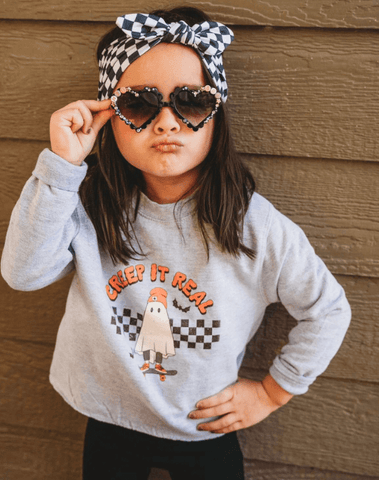 Toddler girl is wearing a comfortable headband featuring a checkerboard print for little girls from By Bella Boutique. Toddler girl is wearing a comfortable headband featuring a checkerboard print for little girls from By Bella Boutique.