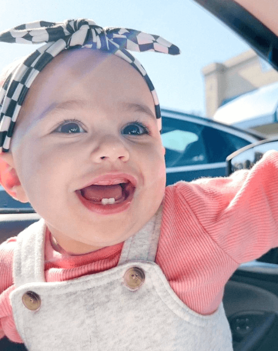 Little girl is wearing a baby head wrap featuring a checkered pattern from By Bella Boutique. Little girl is wearing a baby head wrap featuring a checkered pattern from By Bella Boutique.
