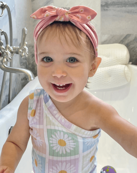 Little girl is wearing a knotted head wrap featuring a smiley pattern from By Bella Boutique. Little girl is wearing a knotted head wrap featuring a smiley pattern from By Bella Boutique.