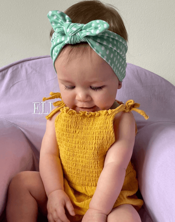 Baby girl is wearing a knotted headband featuring a dot pattern from By Bella Boutique. Baby girl is wearing a knotted headband featuring a dot pattern from By Bella Boutique.