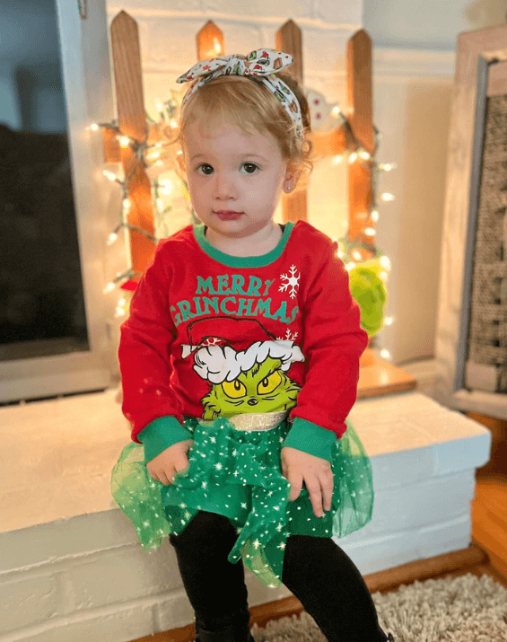 Little girl is wearing a baby head wrap featuring a grinch print from By Bella Boutique. Little girl is wearing a baby head wrap featuring a grinch print from By Bella Boutique.