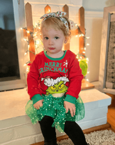 Little girl is wearing a baby head wrap featuring a grinch print from By Bella Boutique. Little girl is wearing a baby head wrap featuring a grinch print from By Bella Boutique.