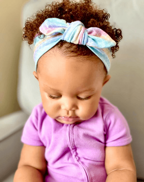Little girl is wearing a baby head wrap featuring a mermaid pattern from By Bella Boutique. Little girl is wearing a baby head wrap featuring a mermaid pattern from By Bella Boutique.