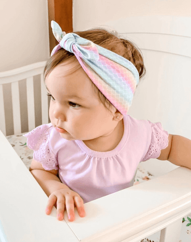 Baby girl is wearing a baby head wrap for little girls featuring a mermaid print from By Bella Boutique. Baby girl is wearing a baby head wrap for little girls featuring a mermaid print from By Bella Boutique.