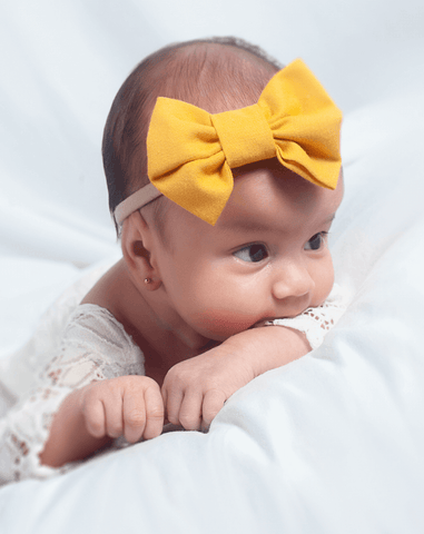 Baby girl is wearing a mustard nylon bow for newborns from By Bella Boutique. Baby girl is wearing a mustard nylon bow for newborns from By Bella Boutique.