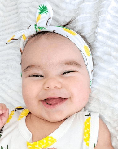 Baby girl is wearing a knotted head wrap featuring a fruit pattern from By Bella Boutique. Baby girl is wearing a knotted head wrap featuring a fruit pattern from By Bella Boutique.