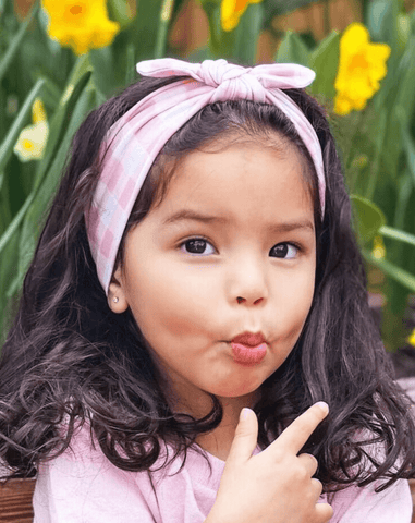 Toddler girl is wearing a pink gingham print top knot headband from By Bella Boutique. Toddler girl is wearing a pink gingham print top knot headband from By Bella Boutique.