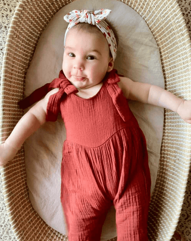 Baby girl is wearing a knotted headband featuring a red floral pattern from By Bella Boutique. Baby girl is wearing a knotted headband featuring a red floral pattern from By Bella Boutique.