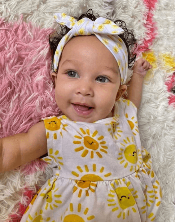 Baby girl is wearing a knotted head wrap featuring a sun print from By Bella Boutique. Baby girl is wearing a knotted head wrap featuring a sun print from By Bella Boutique.