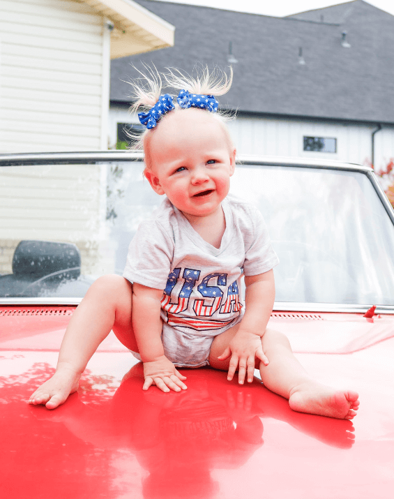 Toddler girl is wearing a set of bow clips featuring a fourth of july pattern from By Bella Boutique.