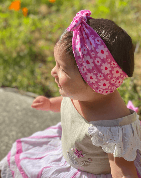 Baby girl is wearing a baby headband featuring a barbie print for little girls from By Bella Boutique.