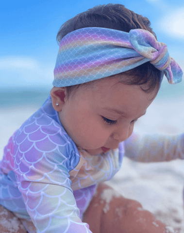 Baby girl is wearing a baby headband featuring a mermaid pattern from By Bella Boutique.