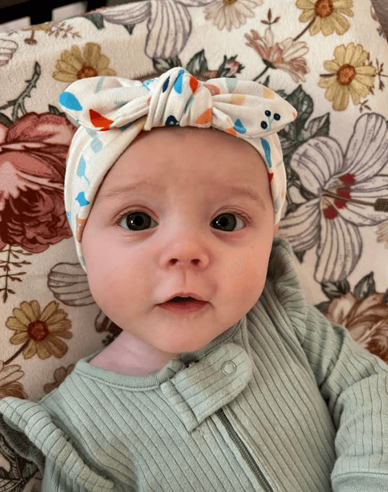 Baby girl is wearing a knotted headband featuring a boho mushroom pattern for little girls from By Bella Boutique.