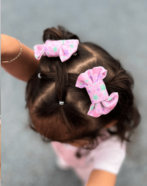 Little girl is wearing a set of handmade clip bows for toddler girls from By Bella Boutique.