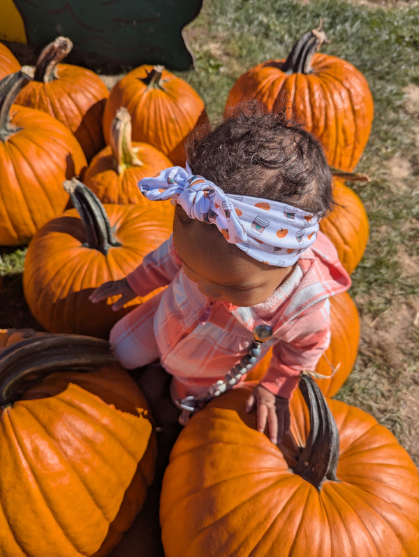 Baby wearing a pumpkin-print headband at a pumpkin patch