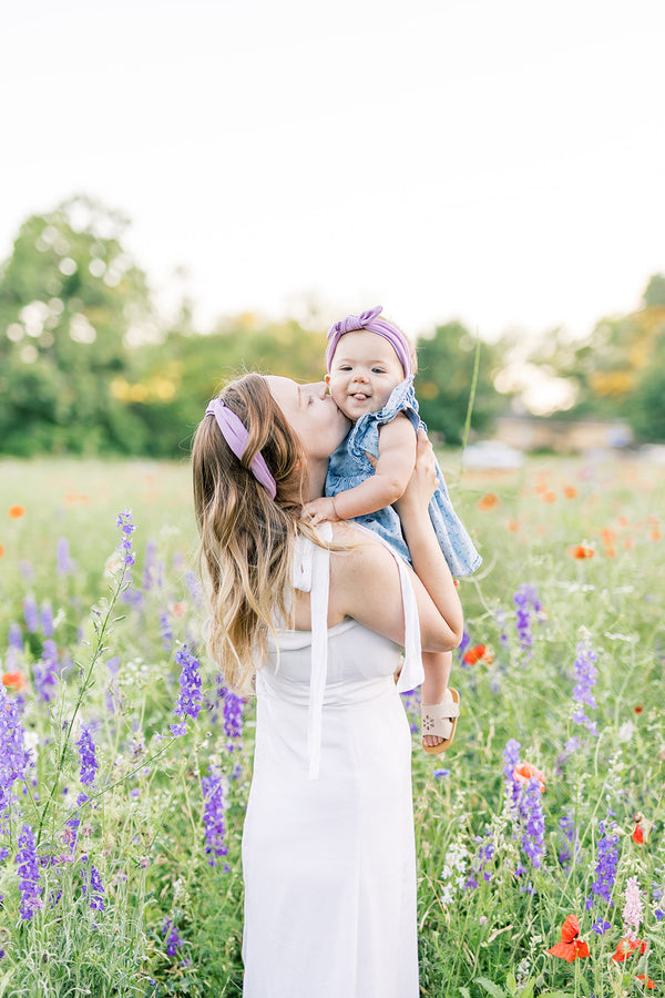 Mom and baby both wearing lavender headbands in a wildflower field