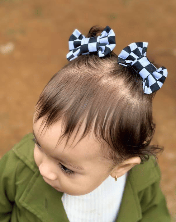 Toddler girl is wearing a set of two hair clips featuring a white checkerboard pattern for little girls from By Bella Boutique.