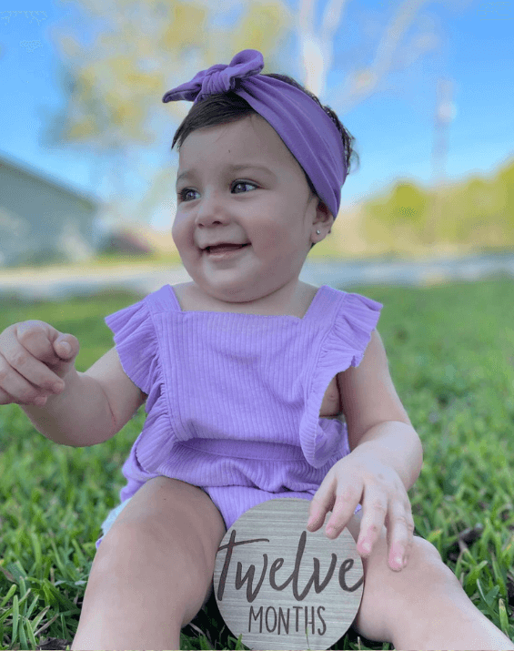 Baby girl is wearing a purple knotted head wrap from By Bella Boutique.