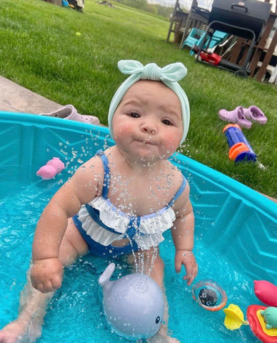 Baby girl is wearing a seafoam color top knot headband for little girls from By Bella Boutique. 