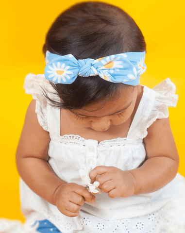 Baby girl is wearing a knotted head wrap featuring a daisy pattern for little girls from By Bella Boutique.