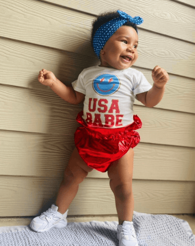 Baby girl is wearing a knotted head wrap featuring a fourth of july pattern for little girls from By Bella Boutique.