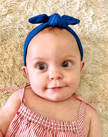 Baby girl is wearing a blue knotted headband for little girls from By Bella Boutique.