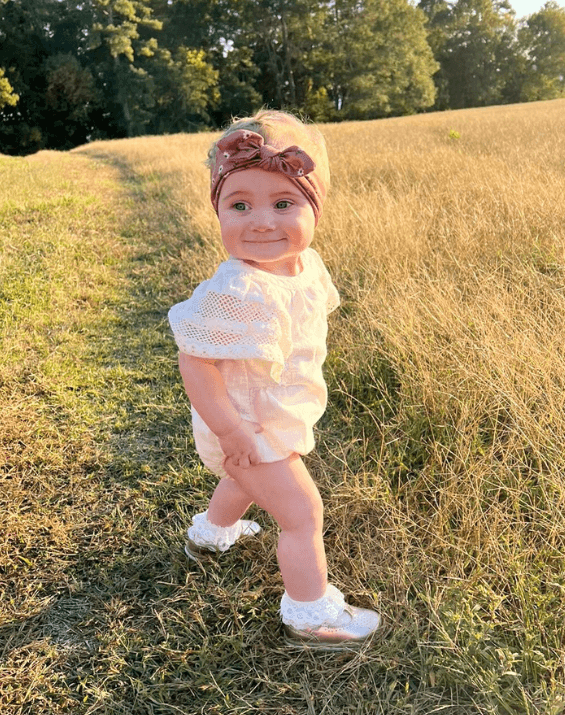 Baby girl is wearing a knotted head wrap featuring a floral pattern from By Bella Boutique.