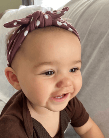 Little girl is wearing a comfortable baby headband featuring a polka dot pattern from By Bella Boutique.