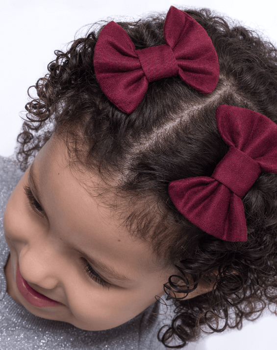 Toddler girl is wearing a set of two burgundy baby pigtail bows from By Bella Boutique. 