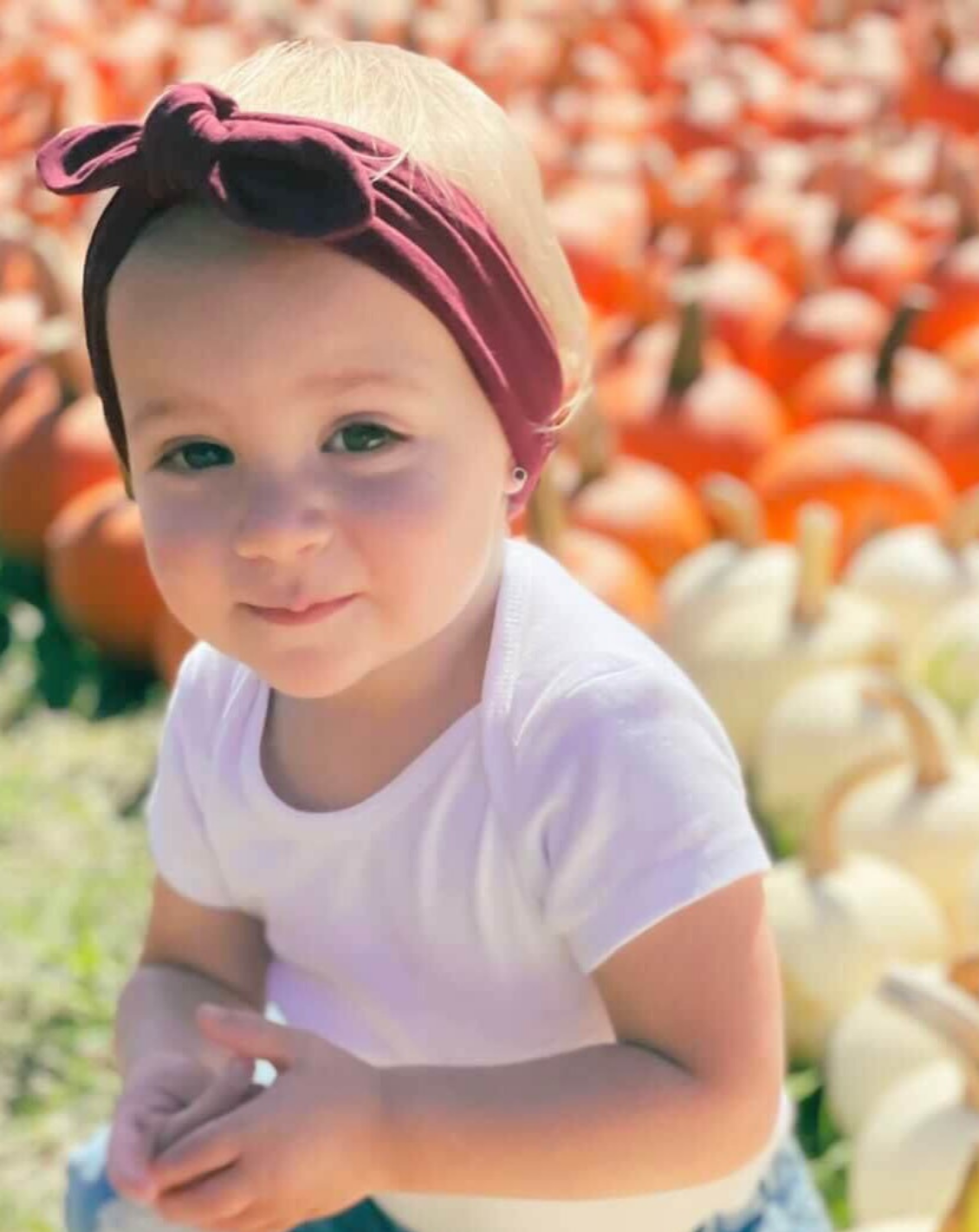 Baby girl is wearing a burgundy top knot headband from By Bella Boutique.