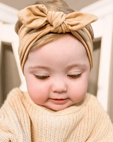 Little girl is wearing a handmade neutral head wrap for girls from By Bella Boutique.