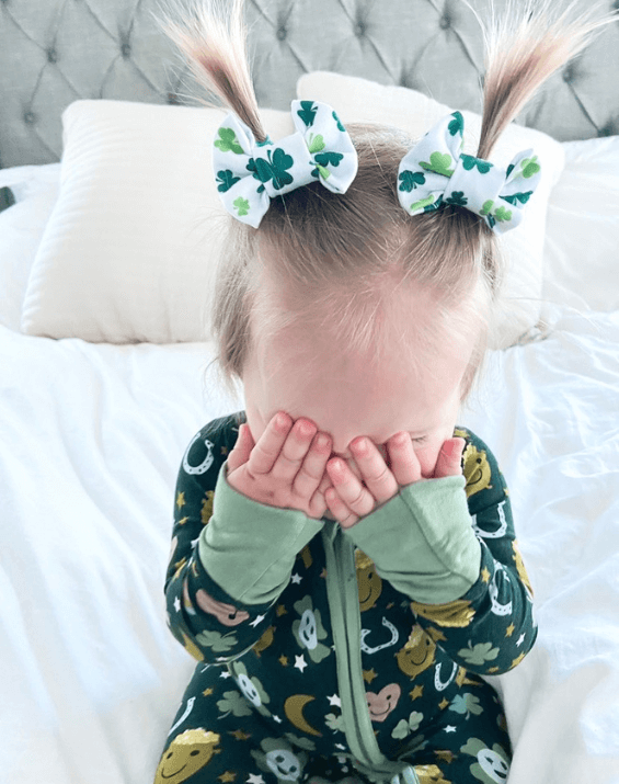 Little girl is wearing a pair of bow clips featuring a shamrock pattern for toddler girls from By Bella Boutique.