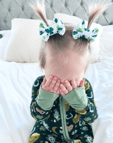 Little girl is wearing a pair of bow clips featuring a shamrock pattern for toddler girls from By Bella Boutique.