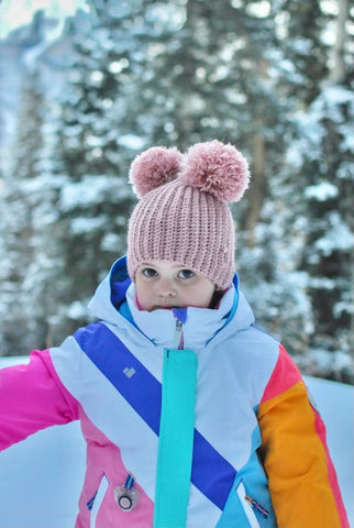 Little girl is wearing a double pom crochet beanie in blush pink from By Bella Boutique.