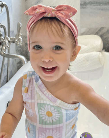 Little girl is wearing a knotted head wrap featuring a smiley pattern from By Bella Boutique.