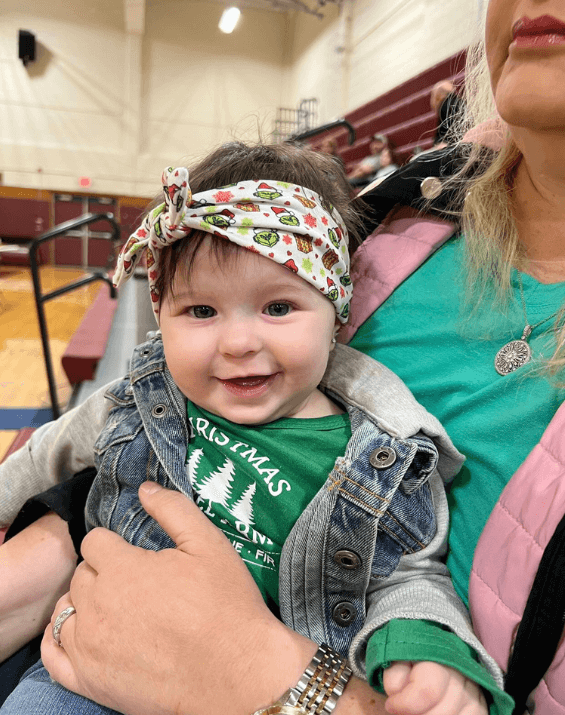 Baby girl is wearing a comfortable headband featuring a grinch print from By Bella Boutique.