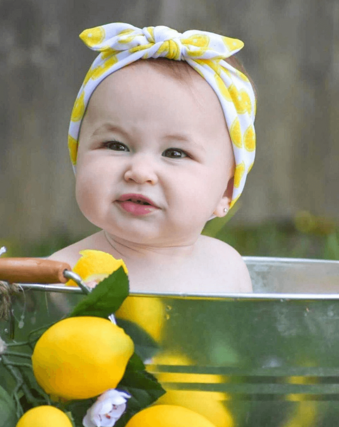 Baby girl is wearing a knotted head wrap featuring a lemon print from By Bella Boutique.