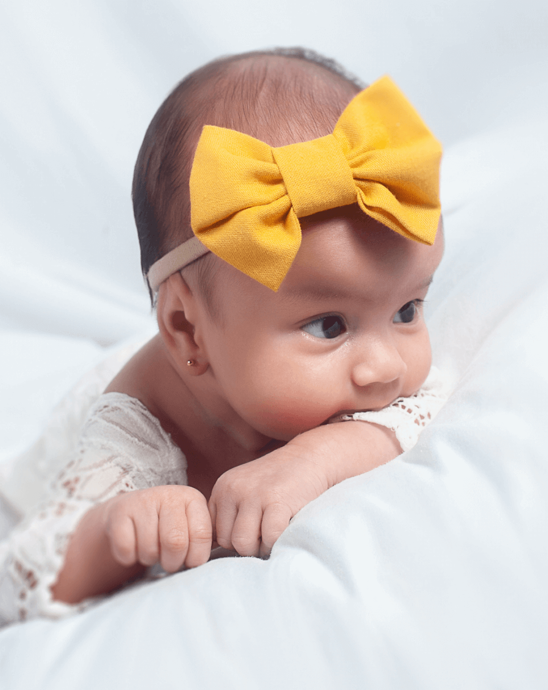 Baby girl is wearing a mustard nylon bow for newborns from By Bella Boutique.