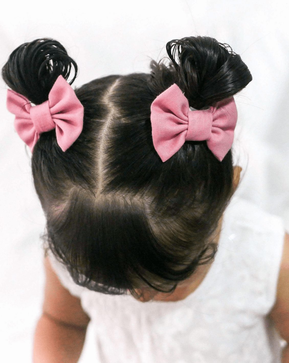 Toddler girl is wearing a set of two pink pigtail bow clips from By Bella Boutique.