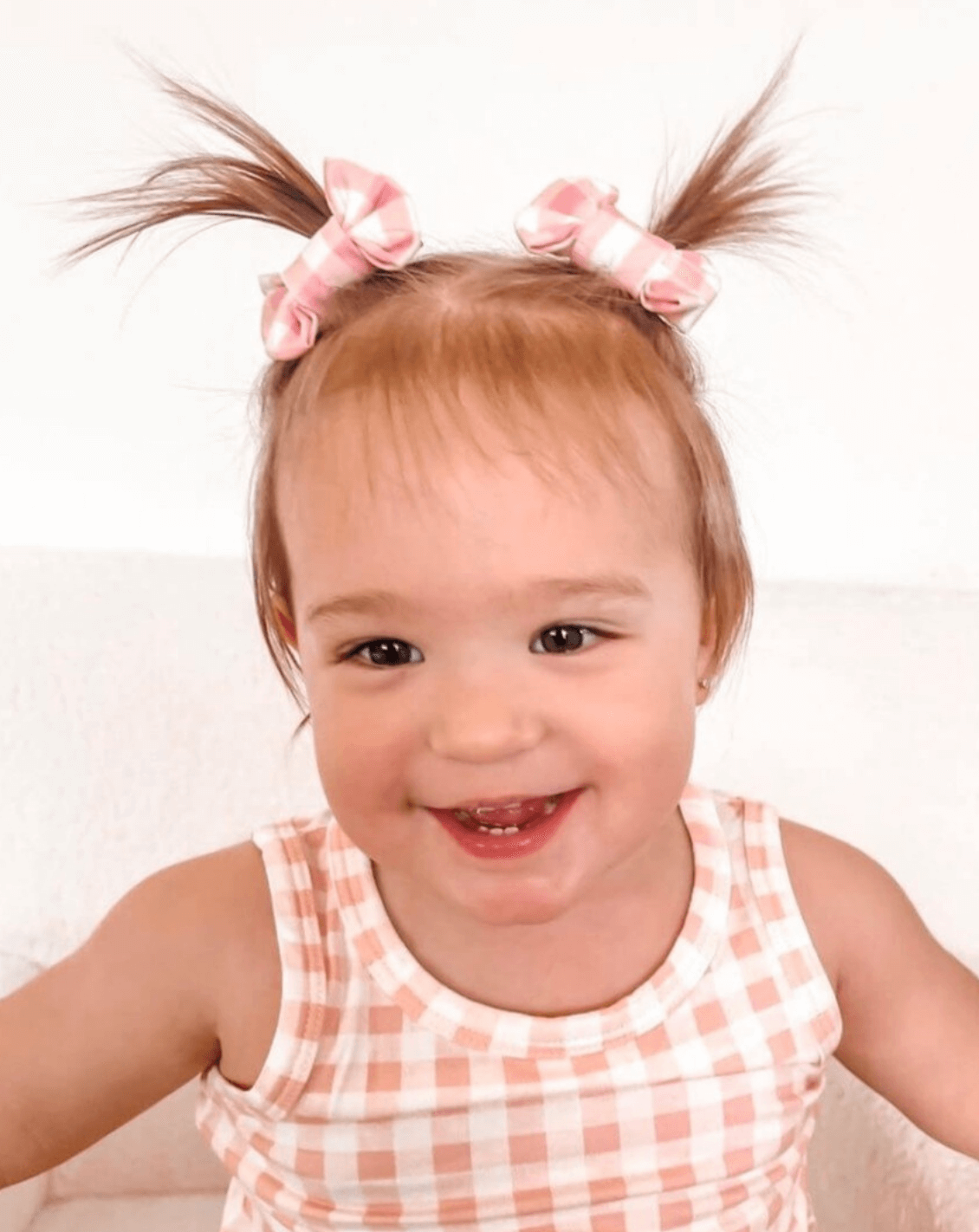 Little girl is wearing a set of two pink gingham print bow clips for toddler girls from By Bella Boutique.