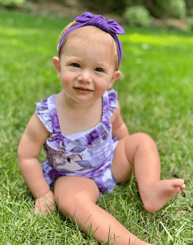 Baby girl is wearing a purple baby head wrap from By Bella Boutique.