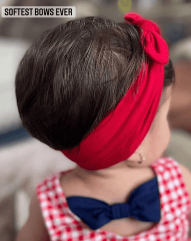 Baby girl is wearing a red top knot headband from By Bella Boutique.