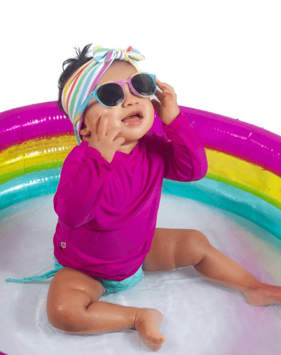 Baby girl is wearing a knotted head wrap featuring a rainbow pattern for little girls from By Bella Boutique.